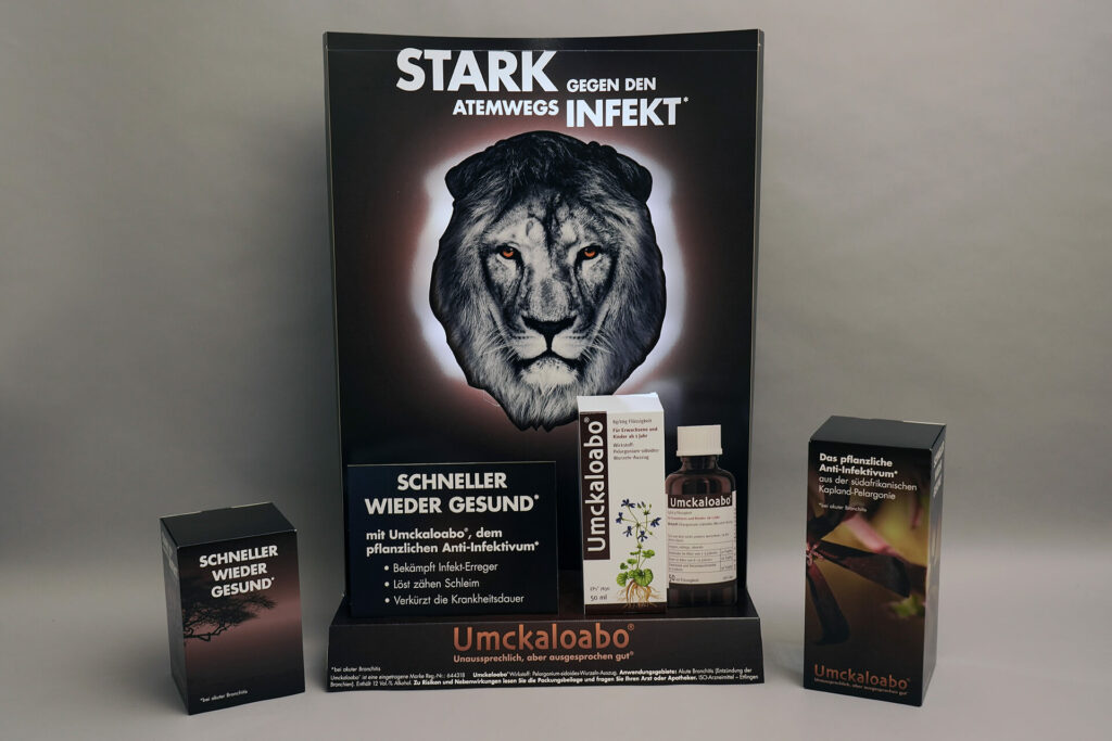 Schaufensterdekoration von pod GmbH für das Medikament Umckaloabo - bestehend aus einem Hauptteil mit der Aufschrift "Stark gegen den Atemwegsinfekt" mit Löwenkopf und der Produktverpackung sowie zwei Rechtecken in unterschiedlichen Größen links und rechts davon